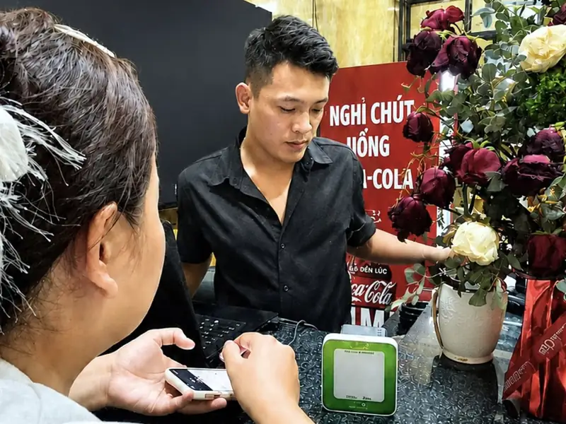 Nhân viên quầy Karaoke Trà Vinh 2 và khách cầm điện thoại thanh toán bên chiếc Loa X Vietcombank